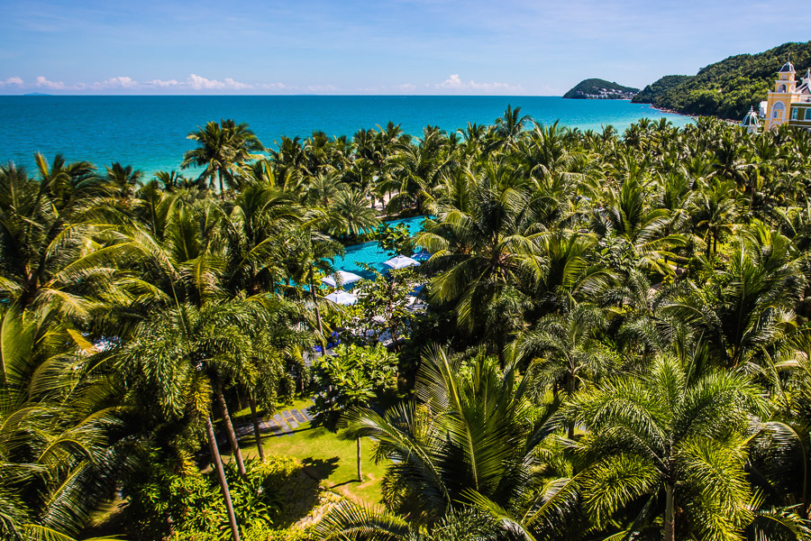 푸꾸옥의 열대 리조트 전경. 울창한 야자수 숲 사이로 푸른 수영장이 보이며, 멀리 에메랄드빛 바다가 펼쳐져 있습니다. 푸꾸옥 숙소 싸게 검색 시 고려해볼 만한 휴양지의 모습입니다.