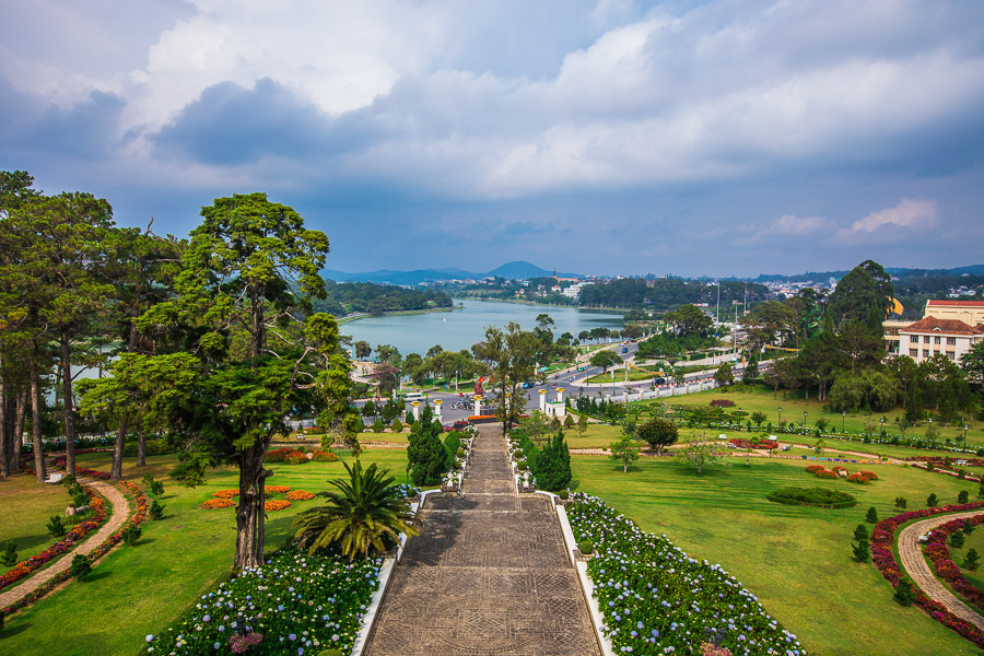 달랏 중심부에 위치한 쑤언흐엉 호수를 배경으로, 아름답게 가꾸어진 공원의 넓은 돌계단이 눈에 띄는 전경. 계단을 따라 푸른 잔디와 다채로운 꽃들이 펼쳐져 있으며, 멀리 호수와 달랏 시가지의 모습이 평화롭게 조화를 이루고 있다.
