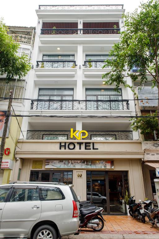 껀터 숙소 싸게 예약할 수 있는 옵션 중 하나인 KP 호텔의 외관입니다. 흰색 건물에 검은색 발코니 난간이 깔끔한 인상을 주며, 호텔 입구 앞에 차량과 오토바이들이 주차되어 있습니다.