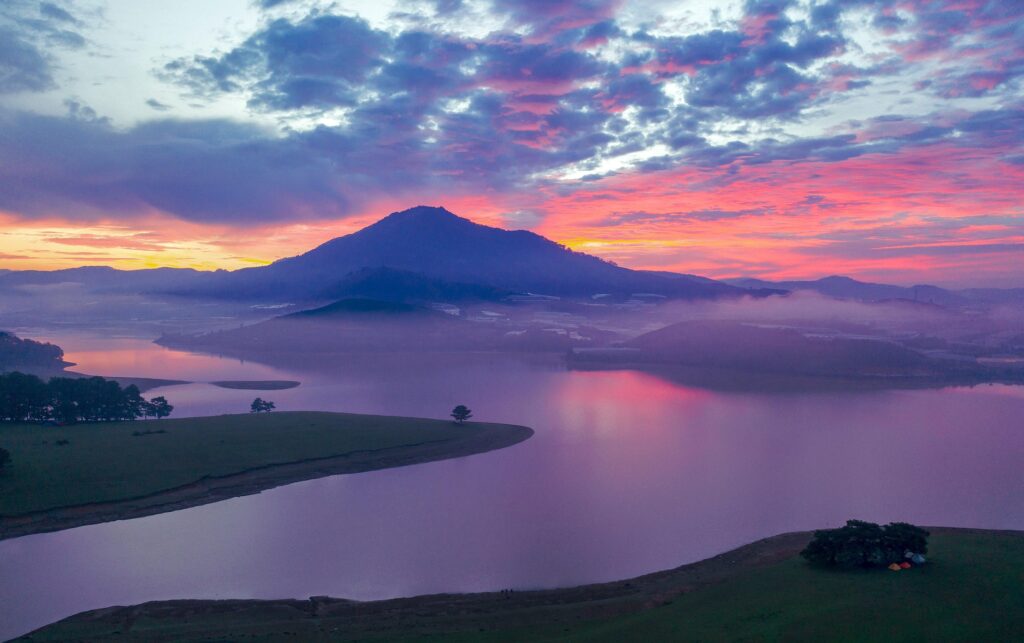 달랏 싸게 여행할 때 만날 수 있는 달랏 새벽 풍경으로, 잔잔한 호수와 보랏빛 하늘, 산 능선 위로 퍼지는 안개가 어우러진 고원 도시 달랏의 자연 전경.