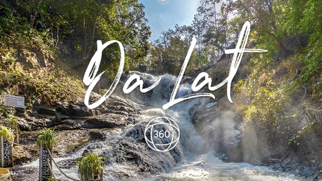초록빛 숲 사이에 있는 달랏의 폭포 전경. 폭포 중앙에 'Da Lat'이라는 흰색 필기체 문구와 360도 아이콘이 겹쳐져 있는 여행 홍보 이미지.